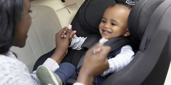 A mother putting her toddler son into a Graco Avolve group 1/2/3 car seat.
